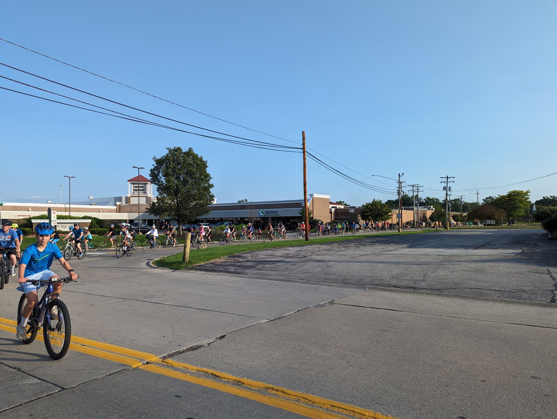 A long line of cyclists riding past the Solon Square shopping plaza during a Bike With a Mayor ride